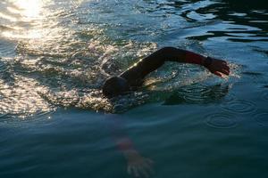 atleta di triathlon che nuota sul lago all'alba indossando la muta foto