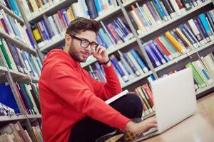 il studenti usi un' taccuino, il computer portatile e un' scuola biblioteca foto