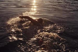 atleta di triathlon che nuota sul lago all'alba indossando la muta foto