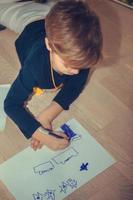 piccolo ragazzo disegno su il carta a casa. foto