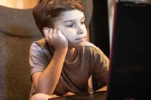 annoiato ragazzo Guardando qualcosa su il Internet al di sopra di il computer portatile. foto