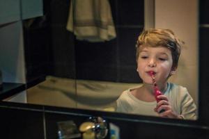 poco ragazzo spazzolatura denti nel il mattina. foto
