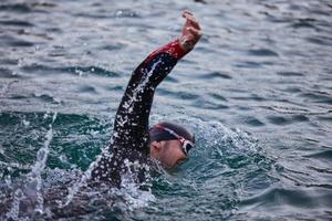 atleta di triathlon che nuota sul lago all'alba indossando la muta foto