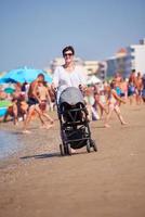 madre a piedi su spiaggia e spingere bambino carrozza foto