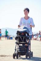 madre a piedi su spiaggia e spingere bambino carrozza foto