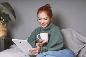 donna rilassante a casa utilizzando tavoletta computer per divertimento o comunicazione e potabile caffè foto