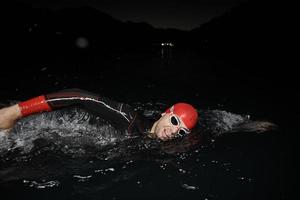 atleta di triathlon che nuota nella notte buia che indossa la muta foto