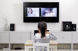 asiatico poco bambino ragazza apprendimento a casa indossare cuffie parlare video chiamata con il computer portatile incontro in linea app, quarantena solitudine durante il coronavirus covid-19 Salute cura, in linea formazione scolastica concetto foto