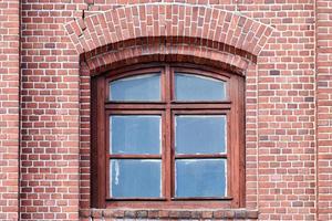 una finestra di vetro ad arco sul vecchio muro di mattoni rossi foto