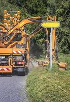 trattore con un' meccanico falciatore falciatura erba su il lato di il asfalto strada. strada Servizi siamo impegnato nel paesaggio in giro strade. verticale Visualizza foto