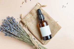 superiore Visualizza di buio bicchiere contagocce bottiglia vith lavanda aromatico essenziale olio o estratto su beige sfondo. mazzo di profumato asciutto lavanda grappolo. pelle e corpo cura cosmetici, aromaterapia foto