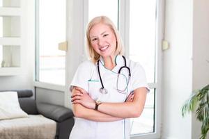 giovane sorridente femmina medico. attraente giovane medico lavoratore. femmina medico braccia incrociato. fiducioso femmina medico in posa nel sua ufficio. avvicinamento di un' femmina medico con stetoscopio foto