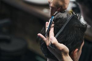 barbiere. avvicinamento di uomo taglio di capelli, maestro fa il capelli messa in piega nel barbiere negozio. avvicinamento, maestro barbiere fa il acconciatura e messa in piega con forbici. concetto barbiere. foto