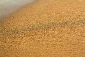 sfondo con d'oro sabbia su il costa di il isola di Creta. astratto superficie con sabbia e chiaro mare acqua per testo. foto