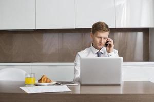 uomo d'affari su chiamata mentre si utilizza il computer portatile al tavolo della colazione