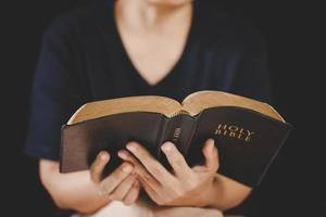 giovane donna persona mano Tenere santo Bibbia con studia a casa. adulto femmina cristiano lettura libro nel Chiesa. ragazza apprendimento religione spiritualità con pregare per Dio. concetto di alunno formazione scolastica fede. foto