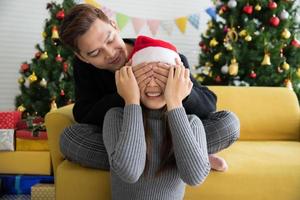 bello uomo preparazione un' Natale presente sorpresa per bellissimo donna nel Santa cappello con chiuso occhi, regalo carta concetto foto