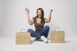 giovane asiatico donna Tenere smartphone e shopping Borsa al di sopra di bianca sfondo studio, shopping e finanza concetto. foto