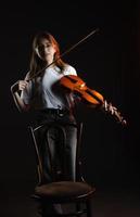 un' ragazza con un' violino su un' buio sfondo, indossare un' bianca maglietta foto