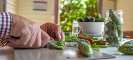 maschio mani nel un' plaid camicia tagliare cetriolo insalata con un' coltello. salutare cibo concetto. vegetariano cibo. orizzontale foto