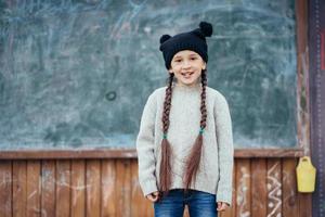 poco ragazza nel un' cappello in posa su il sfondo di il scuola lavagna foto