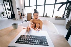 giovane donna Lavorando su il computer portatile mentre assunzione un' vasca da bagno foto