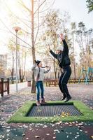 mamma e sua figlia salto insieme su trampolino nel autunno parco foto