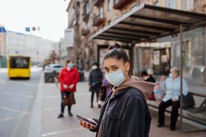 giovane donna indossare chirurgico maschera all'aperto a autobus fermare nel il strada foto