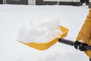 un' uomo spalare il neve di il pala vicino il Casa foto