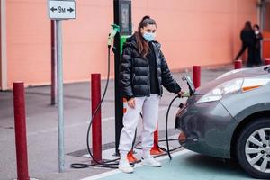 giovane bellissimo donna in viaggio di elettrico auto avendo fermare a ricarica stazione foto