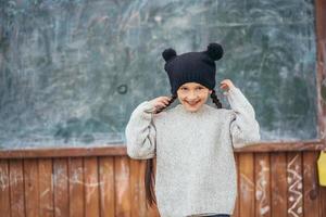 poco ragazza nel un' cappello in posa su il sfondo di il scuola lavagna foto