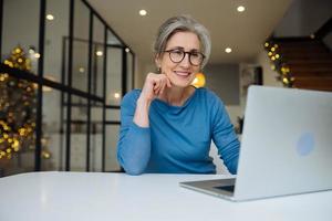 contento maturo mezzo anziano anziano donna guardare a il computer portatile foto