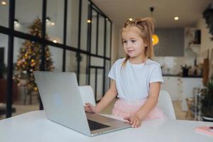 poco ragazza utilizzando tavoletta computer seduta a tavolo foto