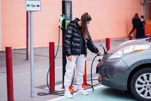 giovane bellissimo donna in viaggio di elettrico auto avendo fermare a ricarica stazione foto