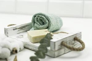 un' bianca macchia mano fatto sapone, un' cotone asciugamano, un' ramo di cotone e verde eucalipto menzogna su un' bianca di legno vassoio foto