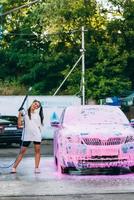 donna con alto pressione tubo flessibile sta di auto coperto nel rosa schiuma foto