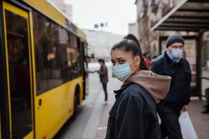 giovane donna indossare chirurgico maschera all'aperto a autobus fermare nel il strada foto