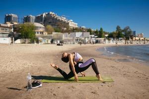 donna fare yoga sta nel un' triangolo posizione su il pubblico spiaggia. foto