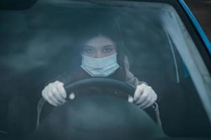giovane donna nel un' maschera e guanti guida un' macchina. foto