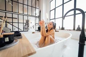 giovane donna dire bugie nel schiumoso bagno rilassa a casa foto