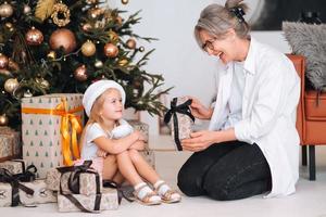 contento nonna dando Natale presente per eccitato nipotina. foto