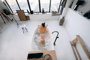 rilassato signora assunzione bagno, godendo e rilassante mentre dire bugie nel vasca da bagno, superiore Visualizza foto