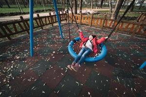 contento bambino ragazza su oscillazione. poco ragazzo giocando nel il autunno pacchetto. foto