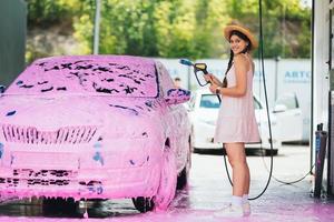 donna con tubo flessibile sta di auto coperto nel rosa schiuma foto