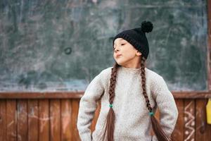 poco ragazza nel un' cappello in posa su il sfondo di il scuola lavagna foto