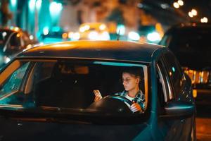 perso femmina autista utilizzando mobile Telefono mentre guida a notte. foto