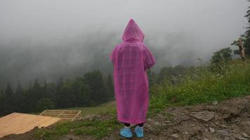 attraente escursionista ragazza nel un' rosa impermeabile sta su un' montagna foto