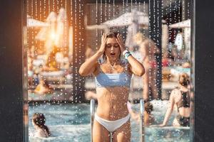 bellissimo ragazza nel costumi da bagno fare la doccia sotto acqua a ricorrere spiaggia. foto