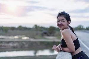 asiatico donna rilassante su un' ponte dopo jogging a tramonto. foto