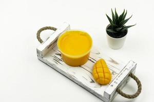 un' Mango giallo mano fatto sapone e un' Mango macchia per corpo cura In piedi su il bianca di legno vassoio nel il moderno bagno foto